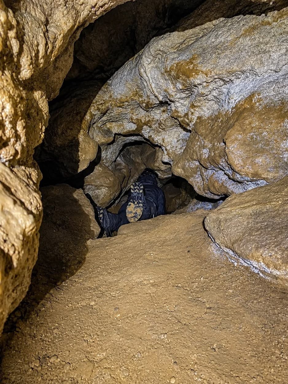 Blick in eine enge Felshöhle mit sandigem Boden